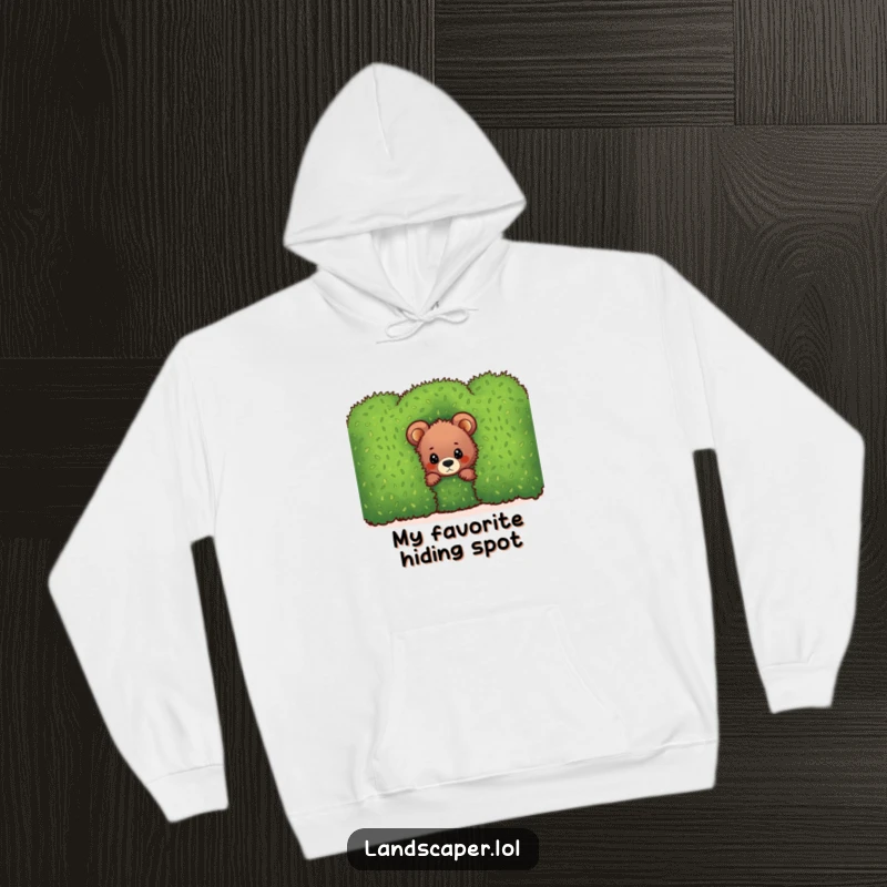 Funny bear cub hoodie, peeking with curiosity from behind a dense, vibrant green hedge, offering warmth and humor.