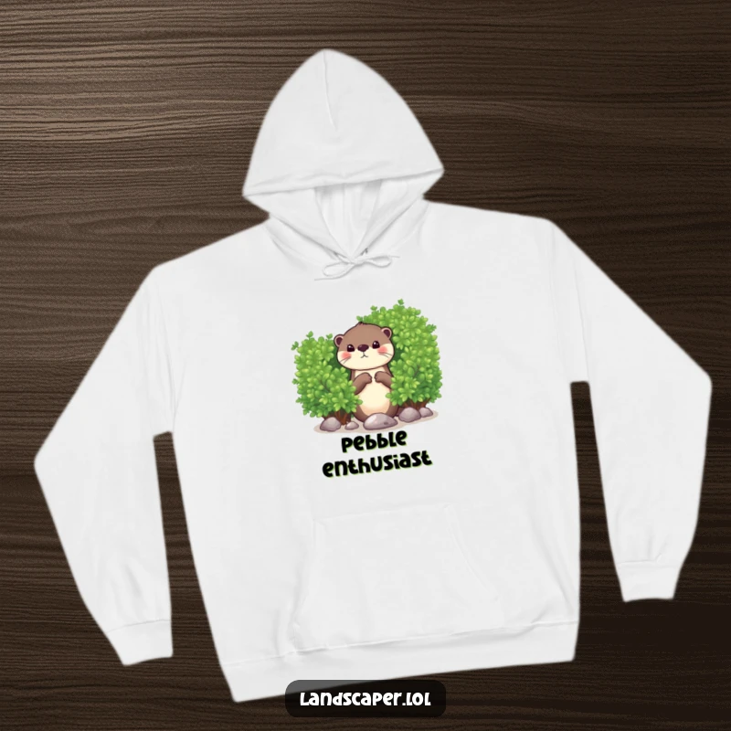 Funny hoodie featuring a curious otter peeking from behind a green bush, playfully dropping a shiny pebble. Cozy and humorous.
